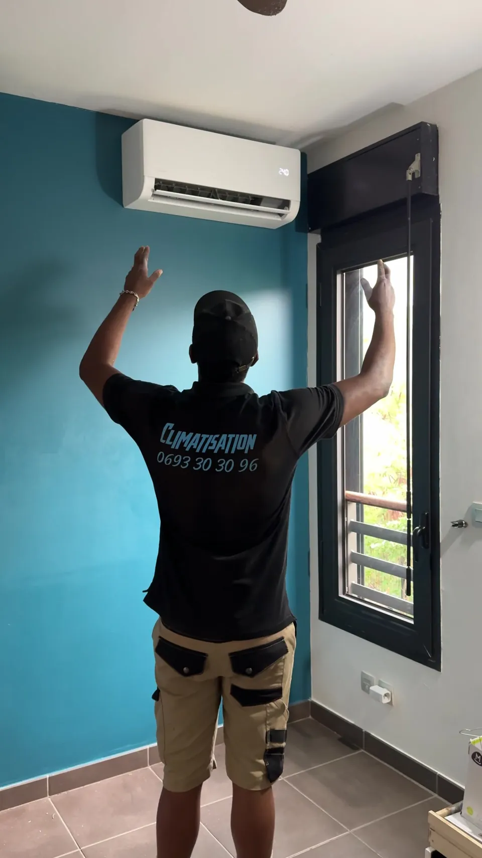 Technicien KLIM-AH bras levés sous une climatisation, avec le 0693 30 30 96 sur son polo